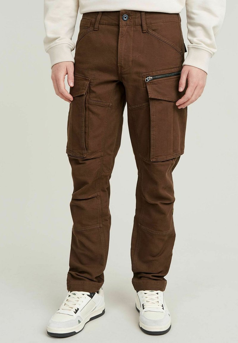 Bruine cargobroek met meerdere zakken, een ritssluitingszak aan de zijkant, stevige stof, taps toelopende benen en een knoopsluiting. Verstelbare tailleband.