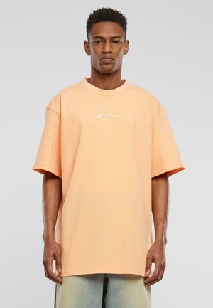 Overmaat t-shirt in licht perzik katoen met een ronde hals en korte mouwen, voorzien van een wit logo ontwerp op de borst.