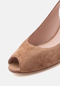 Καφέ σουέντ γόβα με ανοιχτά δάχτυλα, με εσωτερική επένδυση από λείο δέρμα και στρογγυλεμένη άκρη, απεικονίζεται πάνω σε απλό ανοιχτό φόντο.