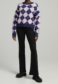 Lila och rosa argyle stickad tröja med vida ärmar, ribbat nederkant och accentknappar, kombinerad med utsvängda svarta byxor och tjocka svarta stövlar.