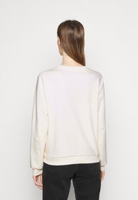 Kremowy sweatshirt z długim rękawem i okrągłym dekoltem. Miękka tekstura o dopasowanym kroju, wyposażony w ściągacze przy rękawach i u dołu.