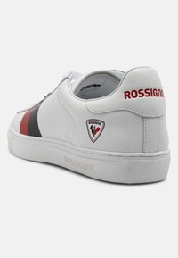 Sneaker bianco con tomaia in pelle liscia, strisce nere e rosse, logo impresso e suola in gomma testurizzata con dettagli a contrasto.
