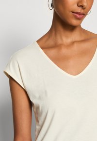 V-hals, T-shirt met korte mouwen in lichtbeige katoen. Zachte textuur met een relaxte pasvorm en een eenvoudig ontwerp, zonder patronen of versieringen.