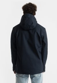 Navy blue hooded jacket with a smooth, matte texture, featuring a relaxed fit and snap closure at the hem, styled with minimalistic design elements.