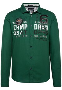 Chemise verte à manches longues avec boutons sur le devant, détails brodés et texte imprimé combinant une typographie audacieuse et des motifs.