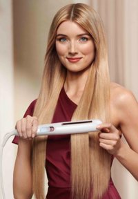 Haard straightener in het wit met een digitaal display, vastgehouden door een persoon met lang, recht, lichtbruin haar, die een bordeauxrode jurk draagt.