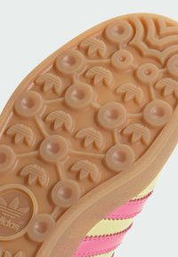 Đonji deo Adidas cipela s teksturiranom gumenom površinom. Ima kružne i listaste uzorke u svetlo smeškastoj boji, obrubljene ružičastim akcentom.