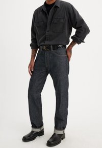 Svart denimskjorta med knäppningar, två bröstfickor; mörkblå löst sittande jeans med gyllene sömmar; svarta läderstövlar med en kraftig klack.