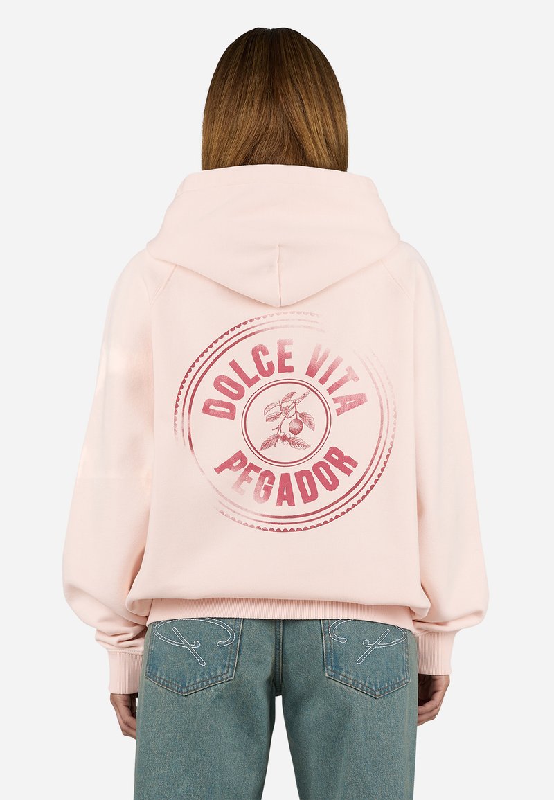 Svijetlo roza hoodie s velikim crvenim kružnim grafičkim motivom na stražnjoj strani, koji uključuje tekst "DOLCE VITA PEGADOR" i botanički dizajn. Opušteni kroj.