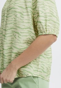 Top a maniche corte in tessuto verde chiaro con motivo ondulato in verde scuro. Polsini elasticizzati e vestibilità rilassata con orlo arrotondato.
