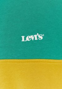 Tissu vert et jaune avec le logo Levi's brodé en blanc sur la partie verte, séparé par une couture.