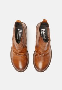 Botas tobilleras de cuero marrón con una textura suave, paneles laterales elásticos y una suela cosida. Diseñadas con una punta redondeada y arrugas sutiles.