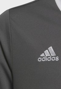 Szara sportowa koszulka z teksturowaną tkaniną, z białym logo Adidas wyszywanym na dolnej lewej stronie oraz zaokrąglonym dekoltem.