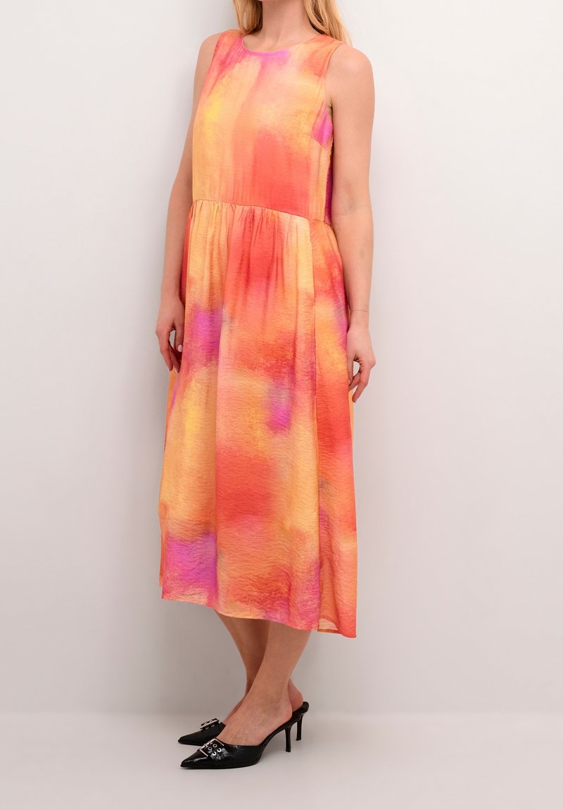 Robe midi sans manches avec taille froncée dans des nuances dégradées orange, rose et jaune, portée avec des mules à talons noires à bout pointu.