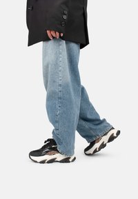 Giacca nera oversize con bottoni, jeans baggy azzurri chiari e sneakers chunky bianche e nere con dettagli in stampa leopardata.