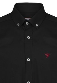 Camisa negra de botones con cuello puntiagudo, botones de contraste blancos y un pequeño bordado de un colibrí rojo en el lado izquierdo del pecho. Textura de tela suave.