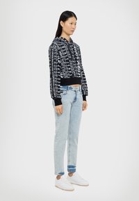Felpa cropped a maniche lunghe bianca e nera con cappuccio regolabile, abbinata a jeans blu chiaro dritti e sneakers bianche.