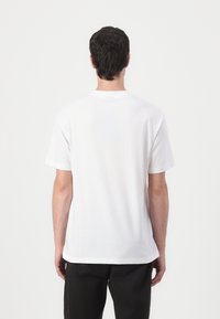 T-shirt branca de algodão com mangas curtas, decote redondo e barra reta. A vista traseira mostra uma textura lisa, sem padrões ou detalhes.