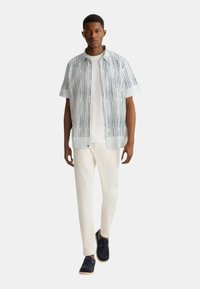 Camicia a maniche corte a fantasia in azzurro chiaro con righe verticali, abbinata a pantaloni bianchi e scarpe blu scuro. Fit e design casual.