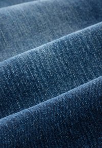 Denim audums ar zilu gradientu, demonstrējot dažādas toņu nianses ar gludu tekstūru un smalkiem auduma rakstiem.