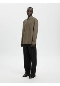 Brun rutete skjorte med knapper, krage, lange ermer og en enkelt brystlomme, kombinert med svarte vide bukser. Svarte sko.