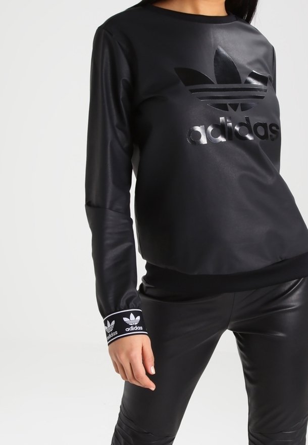 Czarna sportowa bluza z syntetycznego materiału z błyszczącym logo Adidas, okrągłym dekoltem i ściągaczami z białym logo Adidas. Dopasowany krój i faktura.