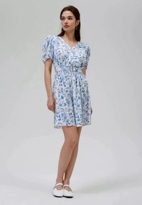 Vestido com estampa floral em azul claro e branco, mangas curtas em balão, decote em V, cintura cintada com um cinto, até ao joelho. Textura de tecido suave.