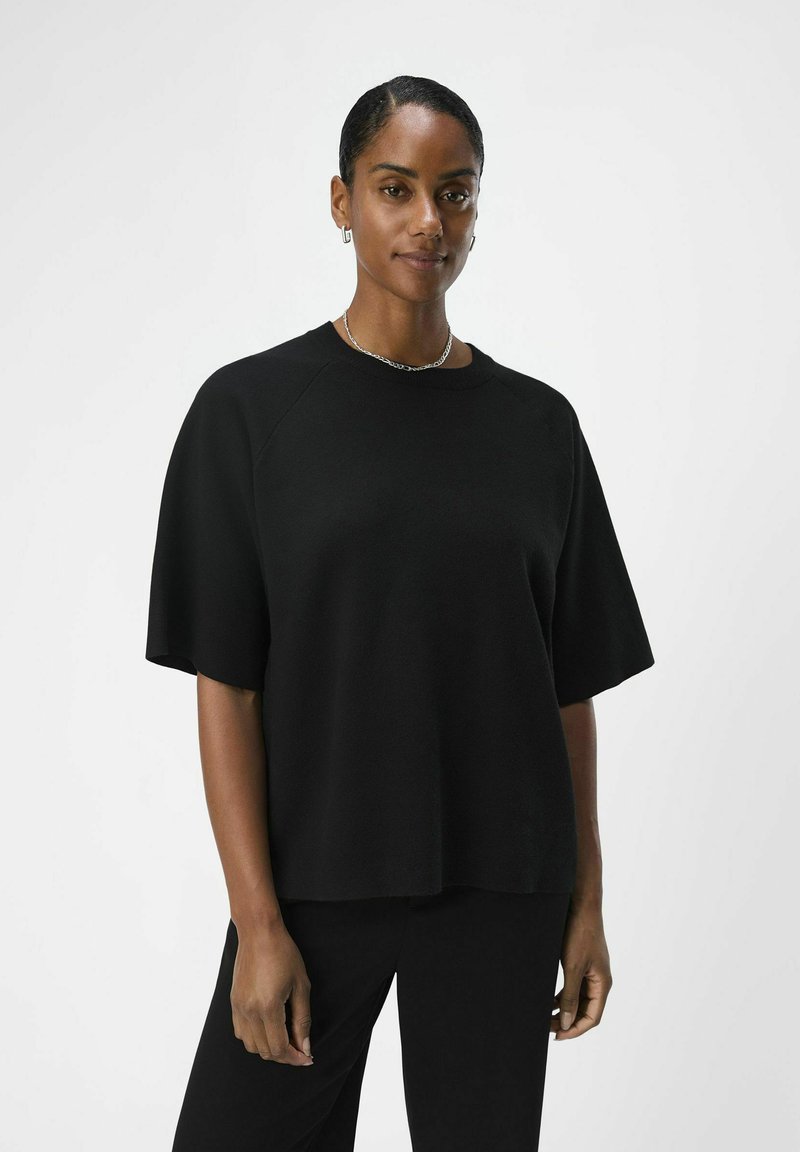 Zwarte oversized top met korte mouwen, gemaakt van zacht materiaal. Heeft een klassieke ronde halslijn en raglanmouwontwerp.