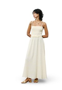 Maxikleid in hellgelber, strukturiertem Stoff mit gerafftem Oberteil, dünnen Trägern und Rüschensaum. Kombiniert mit sandfarbenen Sandalen.