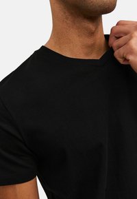 T-shirt in cotone nero con scollatura a V e maniche corte. Tessuto liscio con dettagli di cucitura visibili vicino al collo.