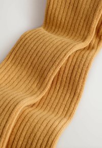 Weiches, strukturiertes, geripptes Gewebe in Hellbraun mit sichtbarem Strickmuster und sanften Falten auf einem einfarbigen, hellen Hintergrund.