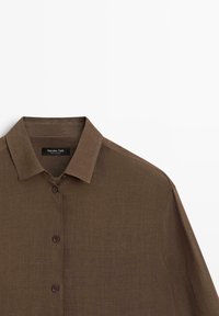 Chemise marron à manches longues avec boutons et col classique, en tissu texturé, présentée sur fond blanc.