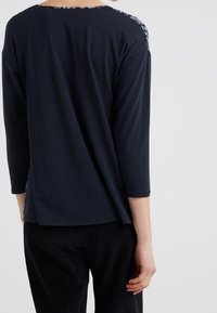 Navy pitkähihaisessa paidassa on kukkakuosi olkapäällä, ja se on väljä ja pehmeästä materiaalista. Asusteena on ribattu musta housut.