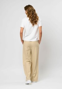 Witte korte mouwen t-shirt gecombineerd met losse, beige wijde broek. Model staat met handen in de zakken en toont de ontspannen pasvorm van de outfit.