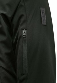 Tessuto di giacca nera con una finitura testurizzata, dotata di una tasca laterale con zip e un'etichetta con il marchio sulla spalla.