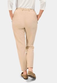 Pantalons beiges au design fuselé, dotés de poches arrière et d'un tissu texturé. Portés avec des chaussures à enfiler marron clair.