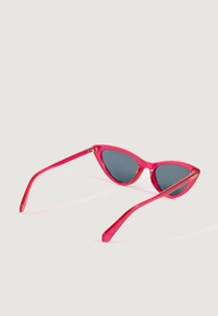 Ružićaste prozirne mačje naočale sa tamnim lećama odložene na običnoj svijetloj površini.