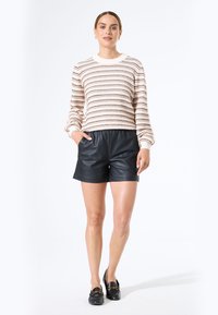 Suéter de punto a rayas en crema, negro y óxido; combinado con pantalones cortos de cuero negros; textura suave; corte relajado; escote redondo clásico.