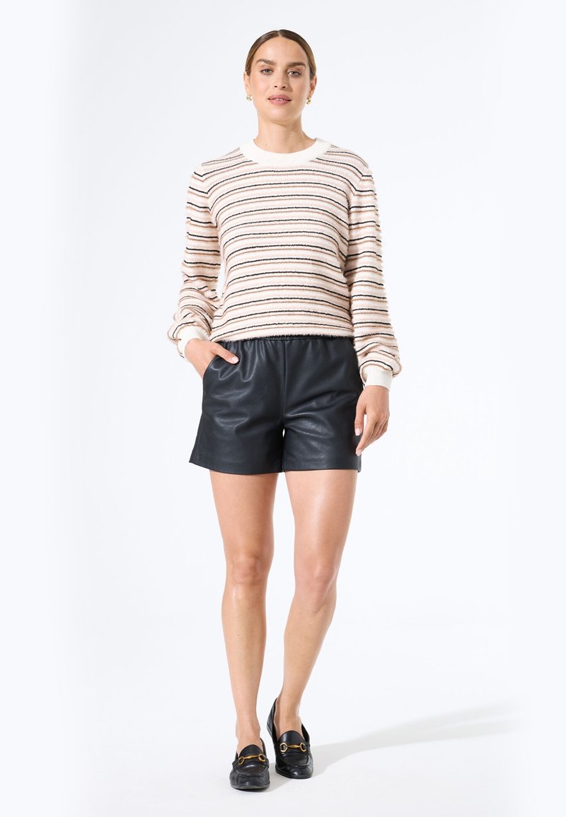 Suéter de punto a rayas en crema, negro y óxido; combinado con pantalones cortos de cuero negros; textura suave; corte relajado; escote redondo clásico.