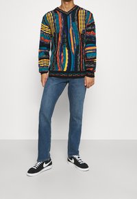 Monivärinen neulepusero, jossa on V-pääntie ja rohkeita raitoja sinisen, keltaisen, punaisen ja vihreän sävyissä. Yhdistetty sinisiin farkkuihin ja mustiin lenkkareihin.