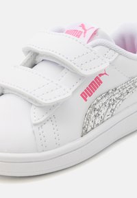 Sneaker in pelle bianca con branding Puma rosa, striscia laterale argentata testurizzata e cinturini in Velcro. Finitura liscia con interno imbottito.