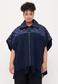 Poncho marin avec un col et des manches matelassés, doté d'une fermeture éclair et d'un ourlet fringé. Fabriqué à partir de matériaux mixtes, offrant un contraste de textures.