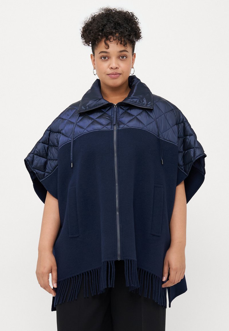 Poncho marin avec un col et des manches matelassés, doté d'une fermeture éclair et d'un ourlet fringé. Fabriqué à partir de matériaux mixtes, offrant un contraste de textures.