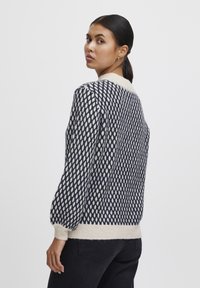 Maglione a maglia con un motivo geometrico blu e crema, polsini a coste e colletto tondo color crema. Tessuto morbido e vestibilità rilassata.