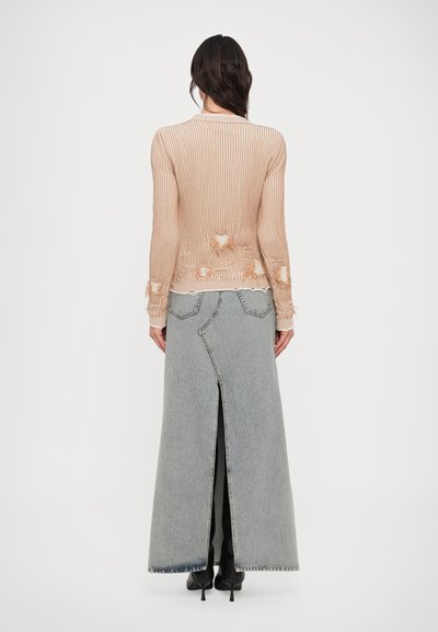 Béžový rebrovaný sveter s ošúchanými detailmi skombinovaný s dlhou sivou denimovou sukňou s predným rozparkom a kontrastným prešívaním.