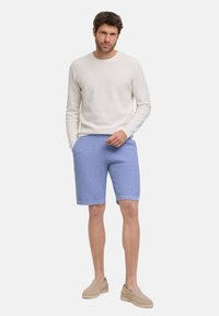 Weißer, strukturierter Pullover kombiniert mit hellblauen Shorts in lässigem Schnitt. Beigefarbene Slipper runden das Outfit ab.