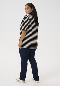 Sort og hvid stribet oversized t-shirt med korte ærmer, kombineret med mørkeblå jeans og hvide sneakers. Glat stoftekstur.