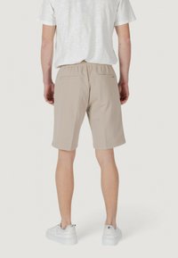 Pantaloni corti beige realizzati in tessuto morbido, con una vestibilità comoda, vita elastica e due tasche posteriori. Indossati con una maglietta chiara e scarpe bianche.