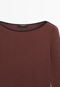 Close-up af en brun ribstrikket langærmet skjorte med rund halsudskæring med sort kant og en synlig Massimo Dutti-label.