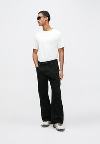 Hvit T-skjorte med korte ermer, svarte vide bukser og grå joggesko. Solbriller fremhever antrekket. Enkelt, avslappet antrekk med moderne snitt.